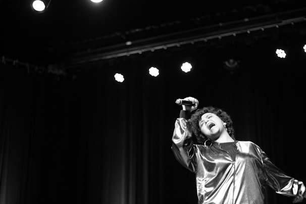 Close-up of Greg Burkimbila passionately singing on stage under golden lights.