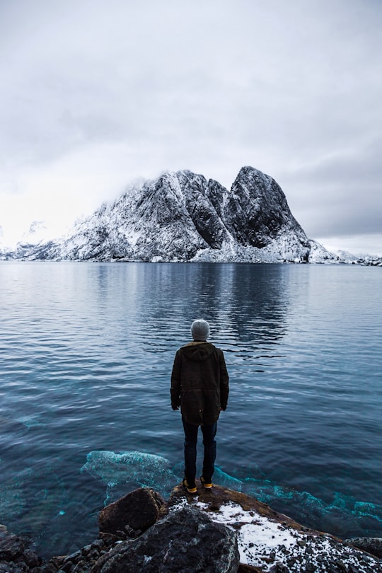 man standing on brown rock near seashore at day time in Hamnøy Norway