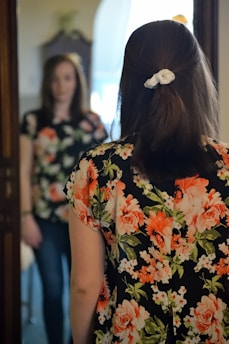 woman wearing black and multicolored blouse and blue denim jeans facing mirror inside white concrete room