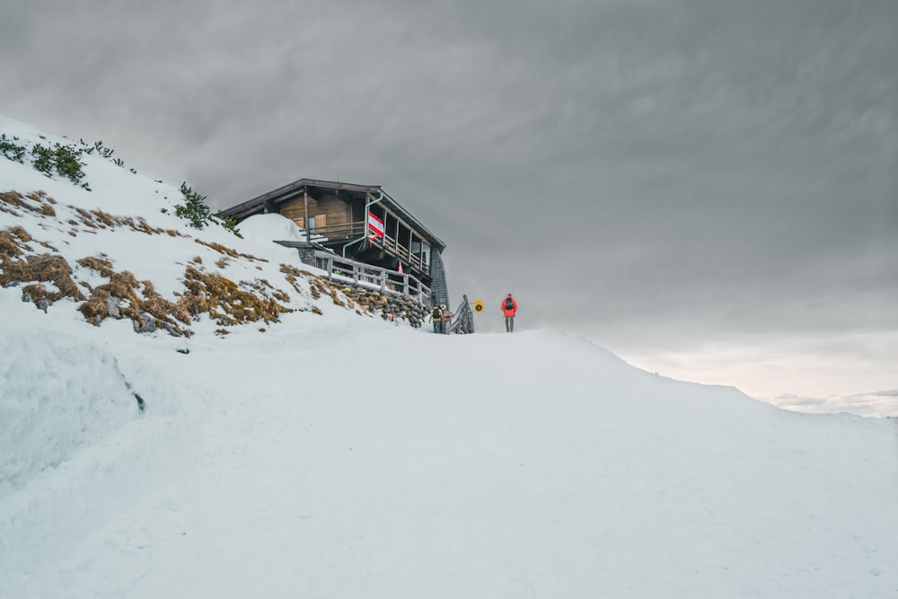 person standing on glacier hill near house under white cloudy skies during winter