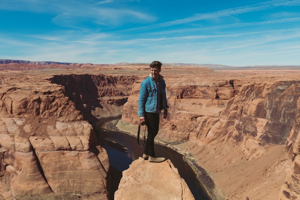 man standing on rocky cliff across hills during daytime