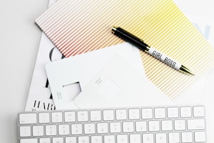 Apple Magic Keyboard, papers, and pen on white surface