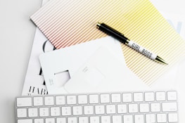 Apple Magic Keyboard, papers, and pen on white surface