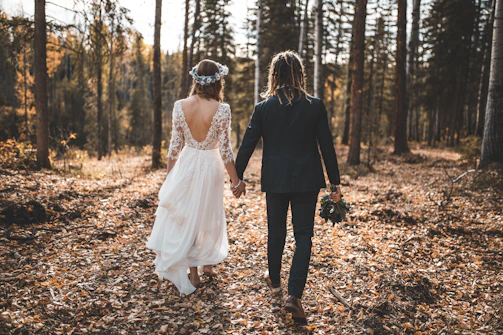 Couple walking hand-in-hand through a sunlit forest during pre-wedding shoot