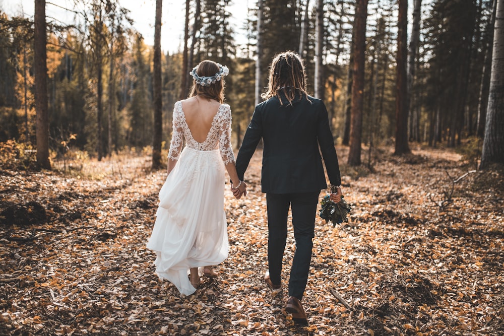 mariée et le marié marchant sur les feuilles couvertes de sol dans les bois pendant la journée