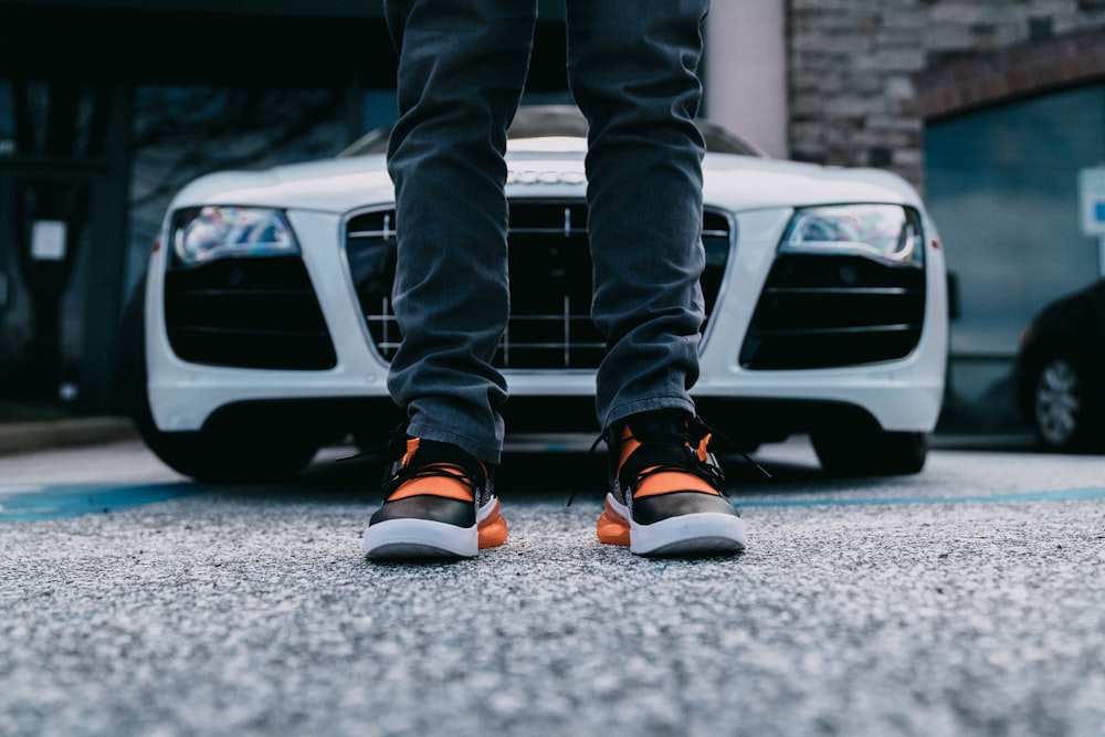 person wearing orange and black shoes behind white car