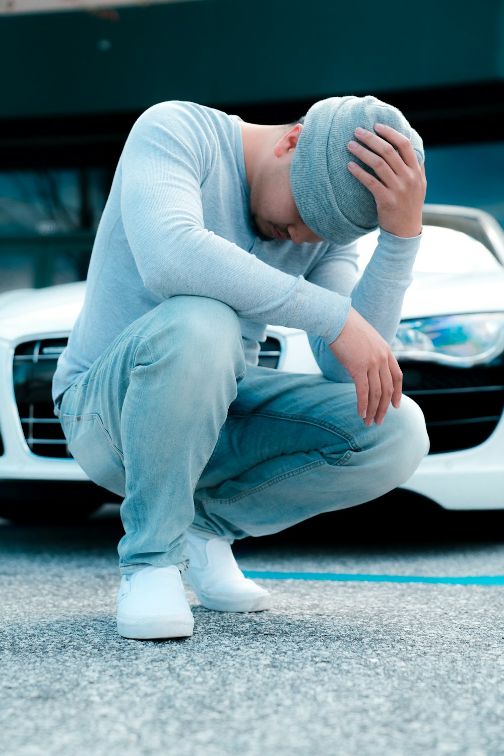 man wearing grey long-sleeved shirt sitting on ground while holding his knit cap