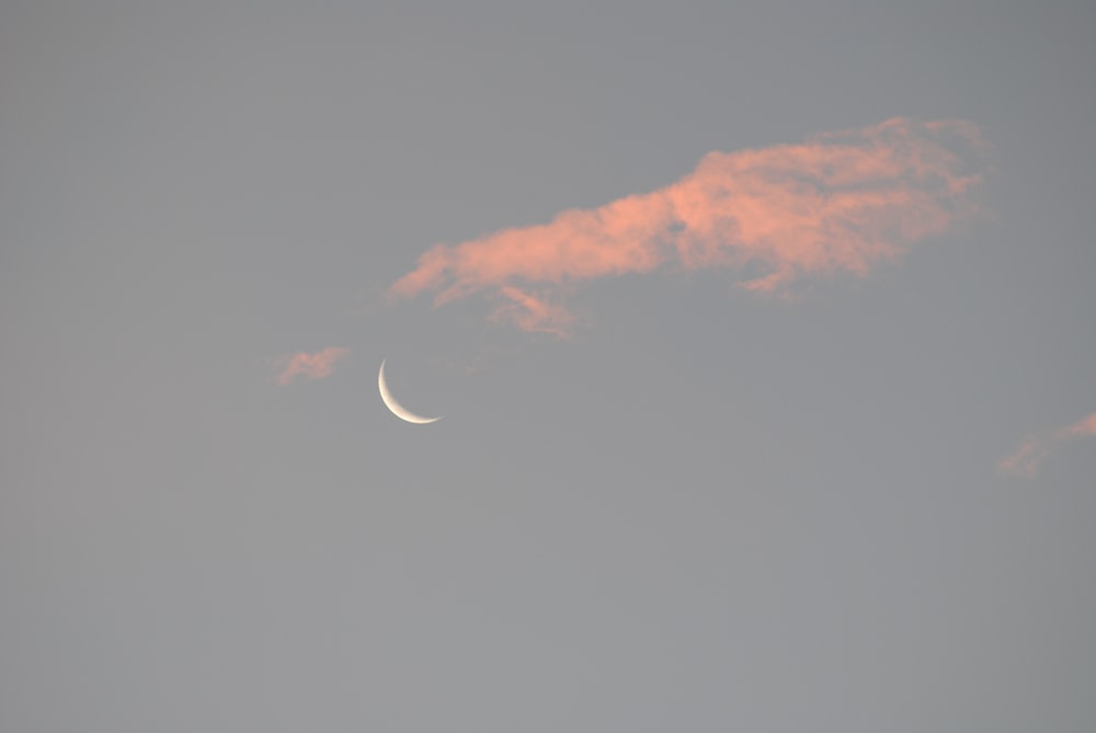 a crescent moon in a cloudy sky with a pink cloud