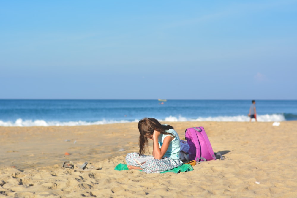 menina senta-se na costa perto da mochila roxa sob o céu azul