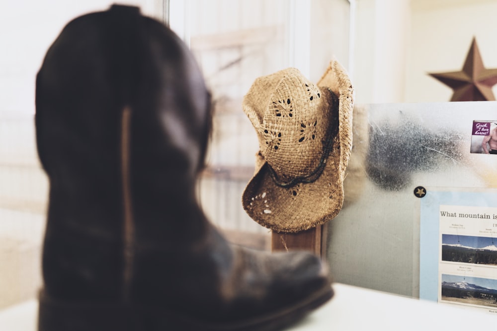 black cowboy boot near brown straw hat on white wall selective-focus photography