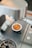 Espresso is being prepared in a metal cup under a professional espresso machine. The coffee has a rich crema on top, and the equipment features a modern, stainless steel design with perforations for drainage.
