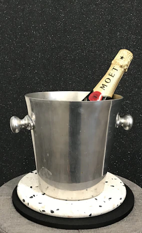 A sleek stainless steel ice bucket with a polished finish, set against a soft gray background.