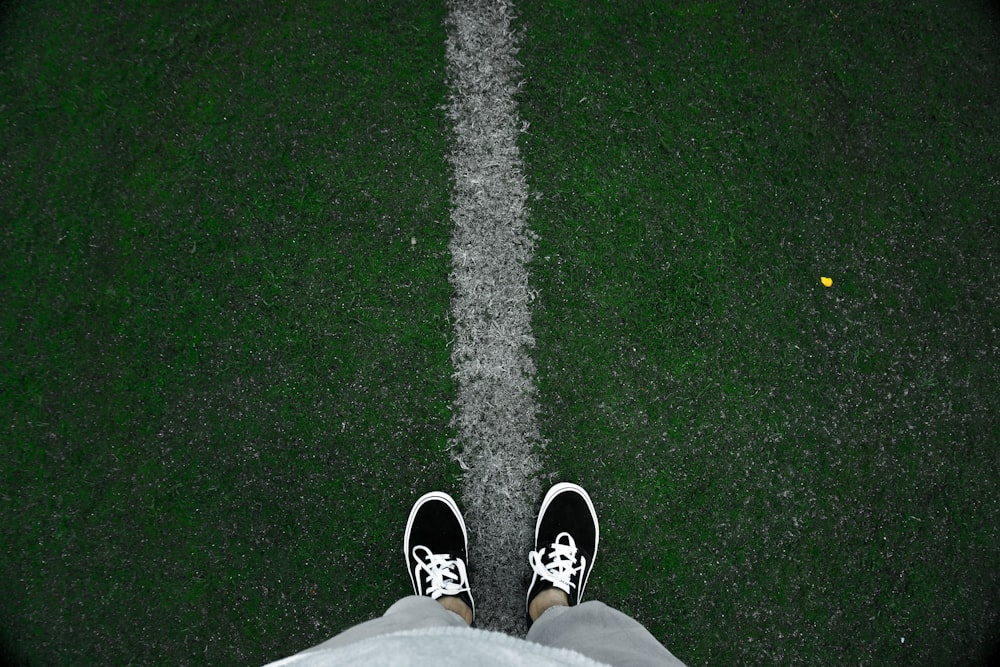 person wearing black low-top sneakers standing on green grass at daytime