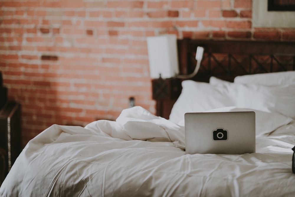 opened gray laptop on white bed comforter near red bricked wall