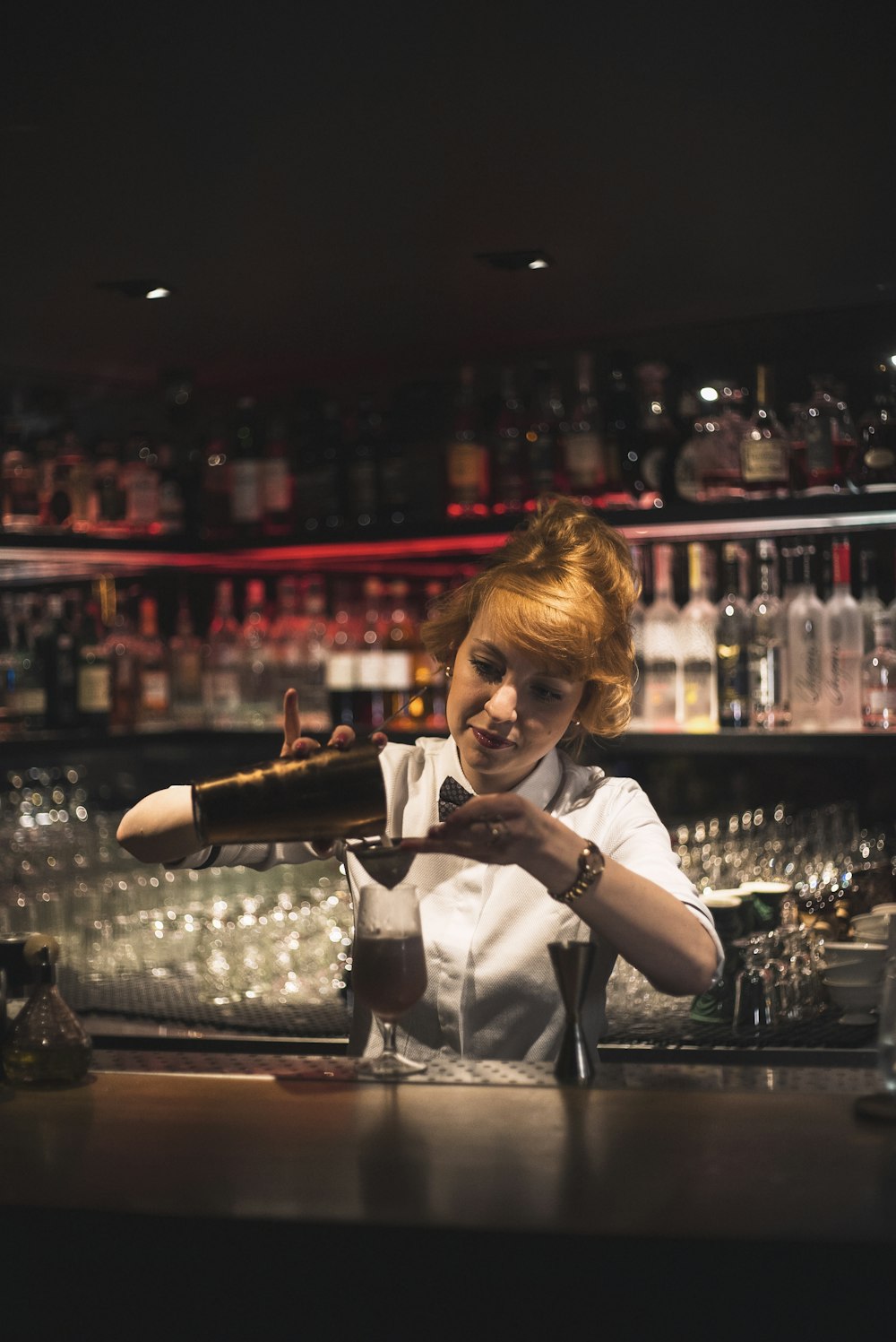 woman pouring bar shaker in clear glass stem glass on bar counter