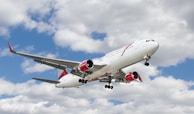white and red flying airplane under white clouds