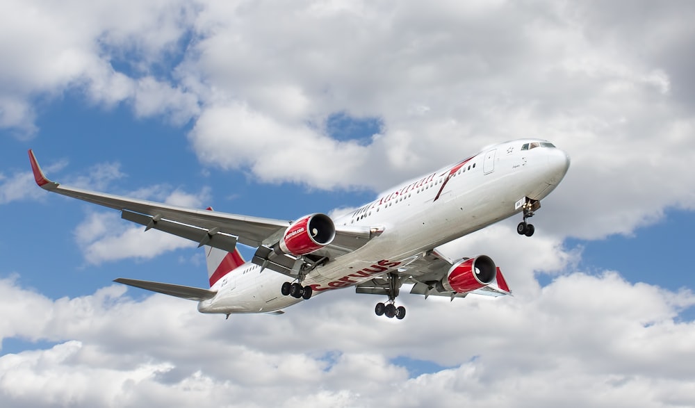 weißes und rotes fliegendes Flugzeug unter weißen Wolken