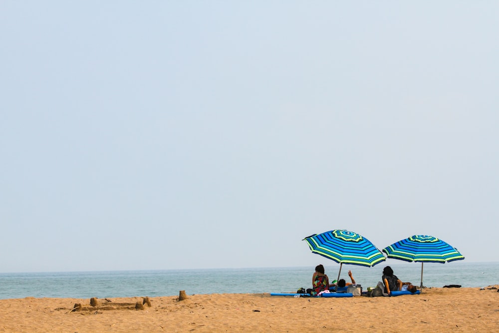 people lying on mat under green and blue umbrella during daytime