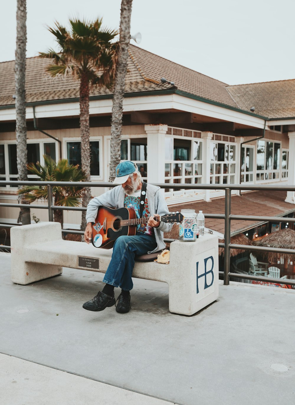 Mann sitzt tagsüber auf einer Bank im Freien und spielt Gitarre