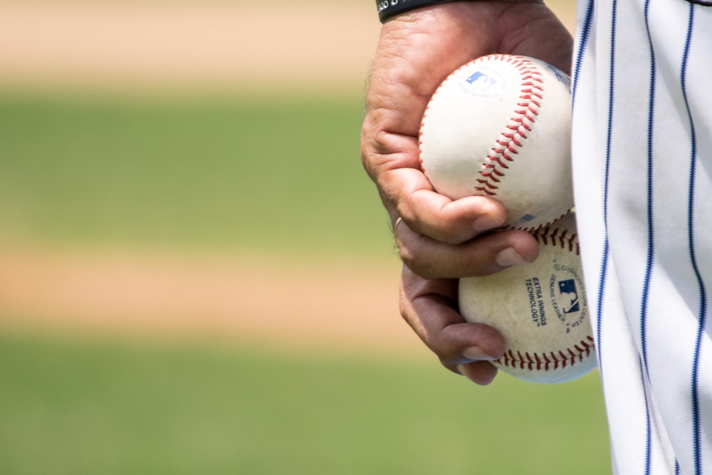 homem segurando duas bolas brancas de beisebol