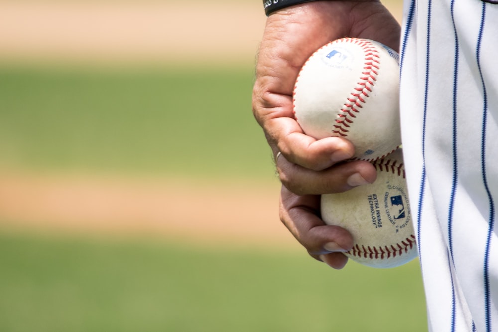 Hombre sosteniendo dos pelotas de béisbol blancas