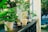 A row of potted plants placed on a balcony railing, featuring various species with lush green and yellow leaves. The background is slightly blurred, showing a garden with trees and grass, capturing a serene outdoor setting.