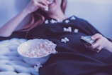 A person relaxing on a couch with popcorn, watching a movie on a tablet.