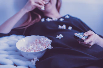A relaxed person enjoying a movie night with popcorn and a laptop.