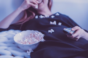 A person relaxing with popcorn and a remote control in hand.