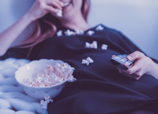 woman lying on bed while eating puff corn