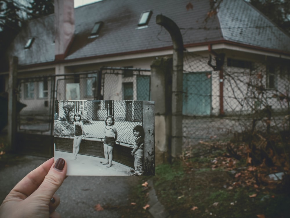 person holding photo of three girls near chainlink fence