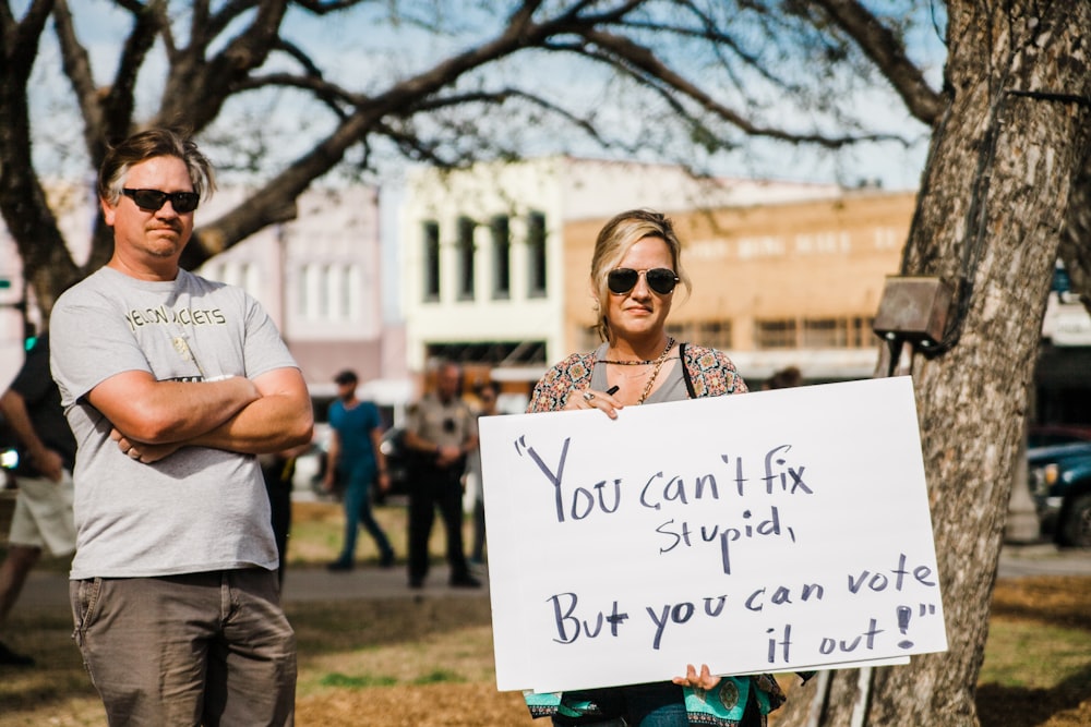 woman wearing sunglasses holding a board with you can't fix stupid, buy you can vote it out print