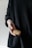 A person wearing a dark, textured sweater holds a cookie in their open hand. The cookie appears to be homemade with a rough, uneven texture, suggestive of a wholesome or artisanal bake.