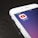 A smartphone screen displaying the YouTube app icon prominently. The phone is resting on a dark wooden surface, with the time and network information visible at the top.