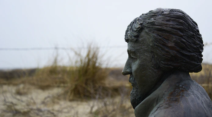Tony of Tucson standing against a weathered desert adobe wall, sunset casting warm amber light highlighting his long white beard.
