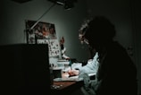 low light photography of woman in gray knit sweatshirt writing on desk