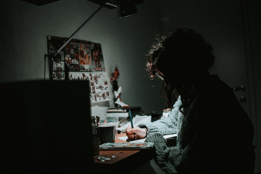 Fotografía con poca luz de mujer en sudadera de punto gris escribiendo en el escritorio