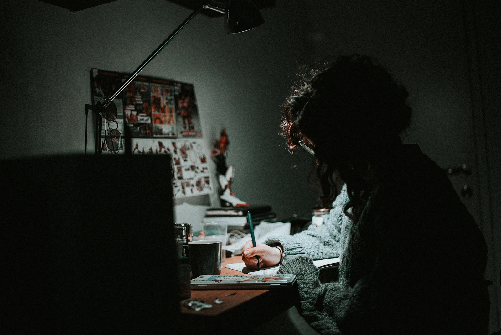 Low light photo of a student in a knit sweatshirt writing at a desk at night