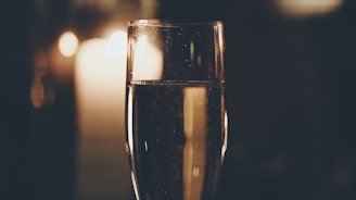 A glass of sparkling champagne is prominently featured, with warm candlelight creating a cozy and intimate backdrop. Tiny bubbles can be seen rising in the glass, adding to the elegant atmosphere.