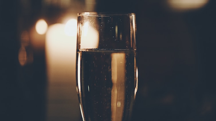 A glass of sparkling champagne is prominently featured, with warm candlelight creating a cozy and intimate backdrop. Tiny bubbles can be seen rising in the glass, adding to the elegant atmosphere.