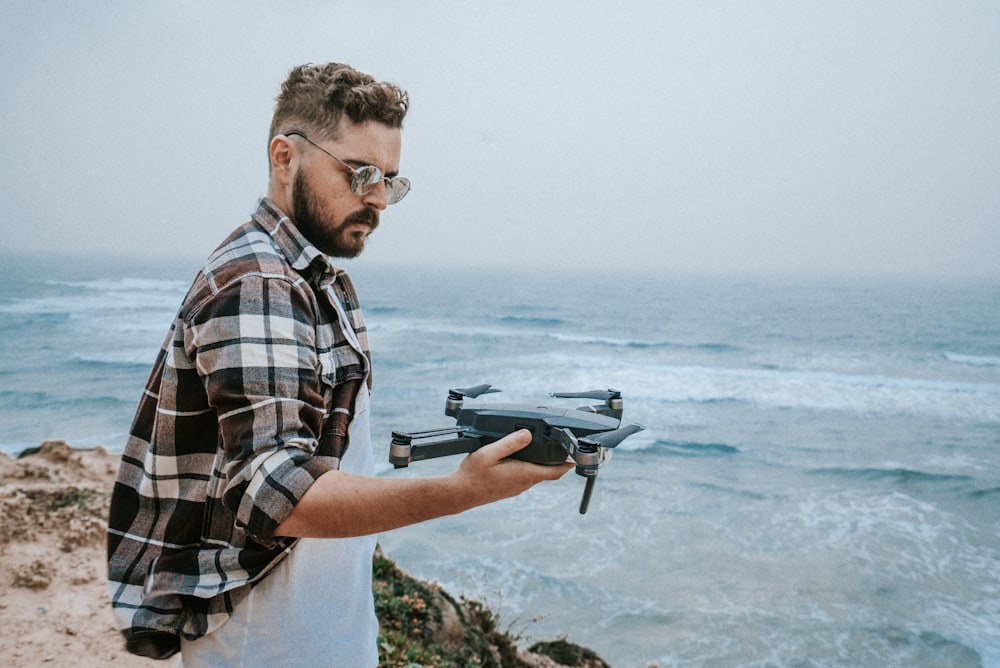 man holding black and brown DJI Mavic Pro drone on his right hand while standing on cliffside with view of sea during daytime photo