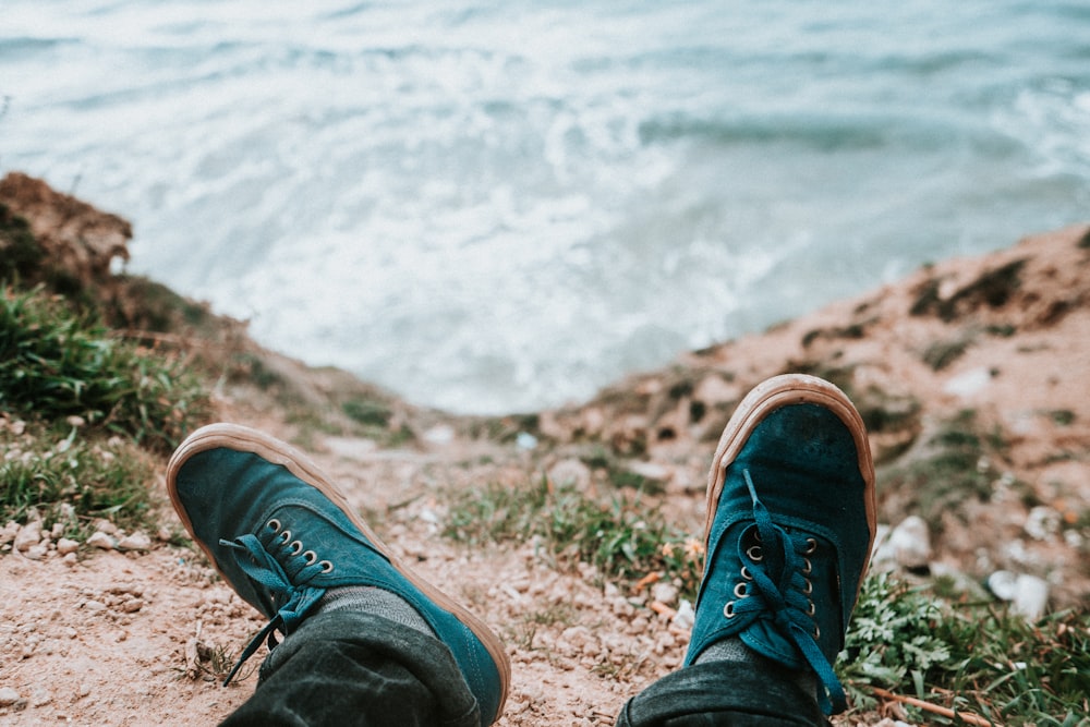 personne portant des baskets basses bleues et brunes devant un plan d’eau