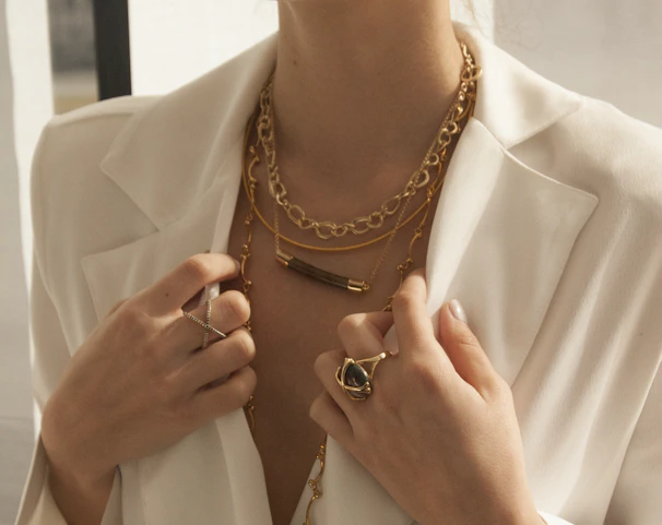 A model wearing layered delicate gold rings and bracelets, styled with a casual streetwear outfit against an urban backdrop.
