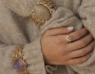 Lifestyle image of a woman’s hand adorned with rings, resting on a cream silk scarf.
