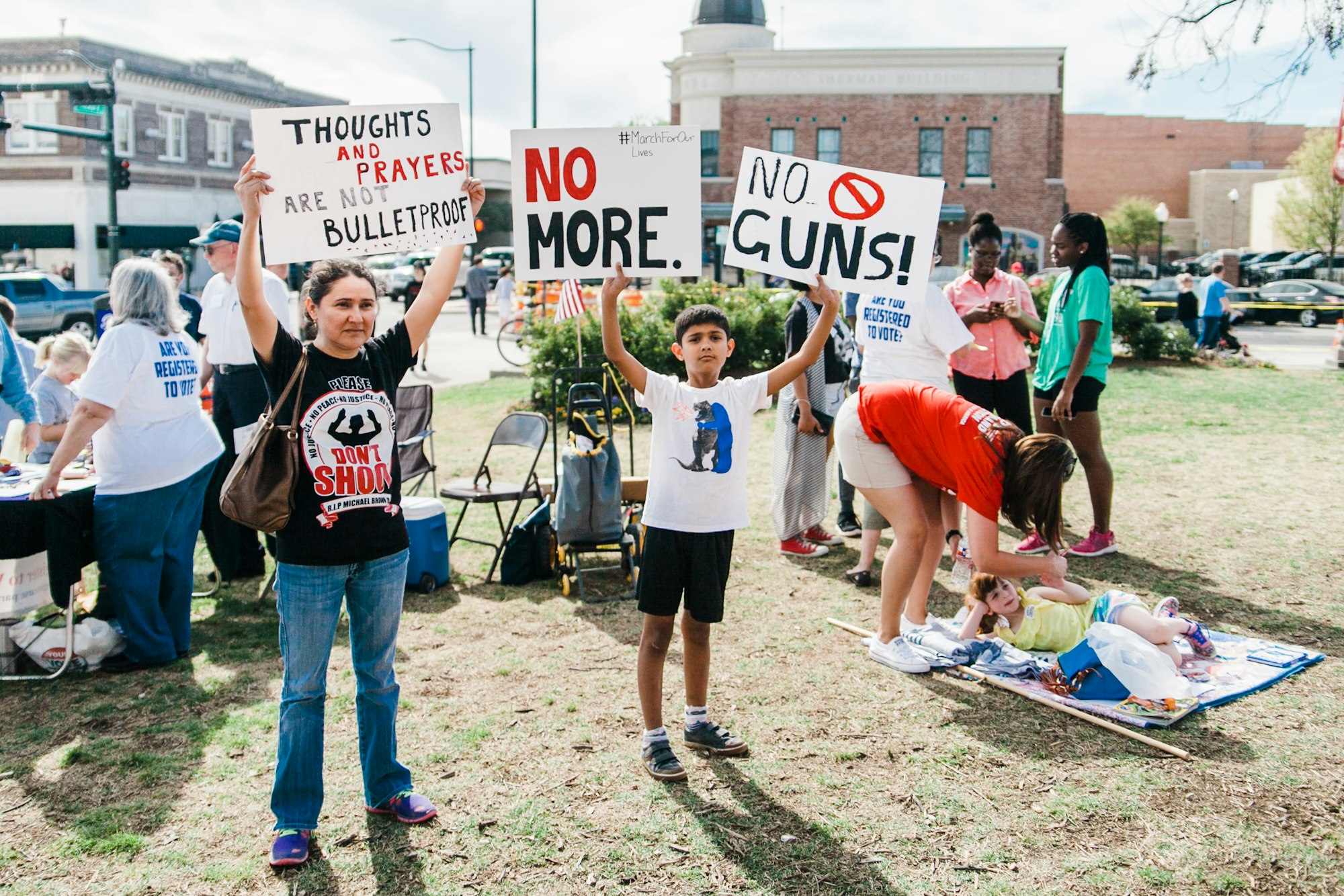 A North Texas mother and her son hold protest signs at the March for Our Lives sister rally in Denton, Texas on March 24th, 2018. In the background, volunteers register people to vote.