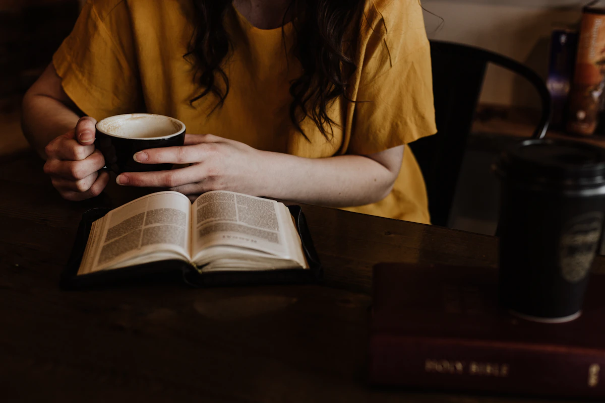 Woman holding a warm mug in front of an open book during quiet morning time