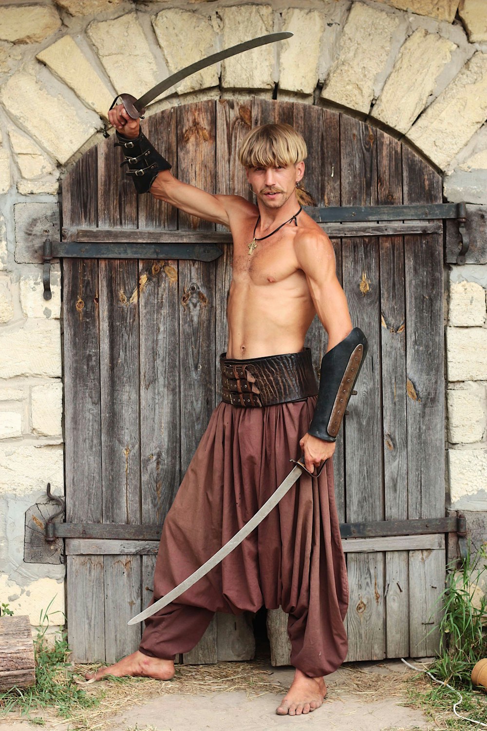 man holding two swords while standing in front of brown gate