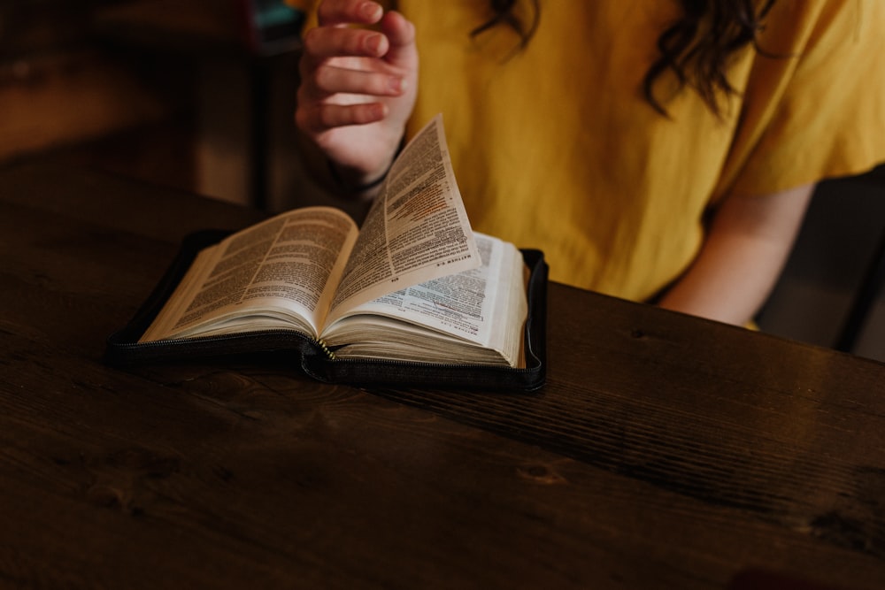 person reading Bible on top of brown wooden table