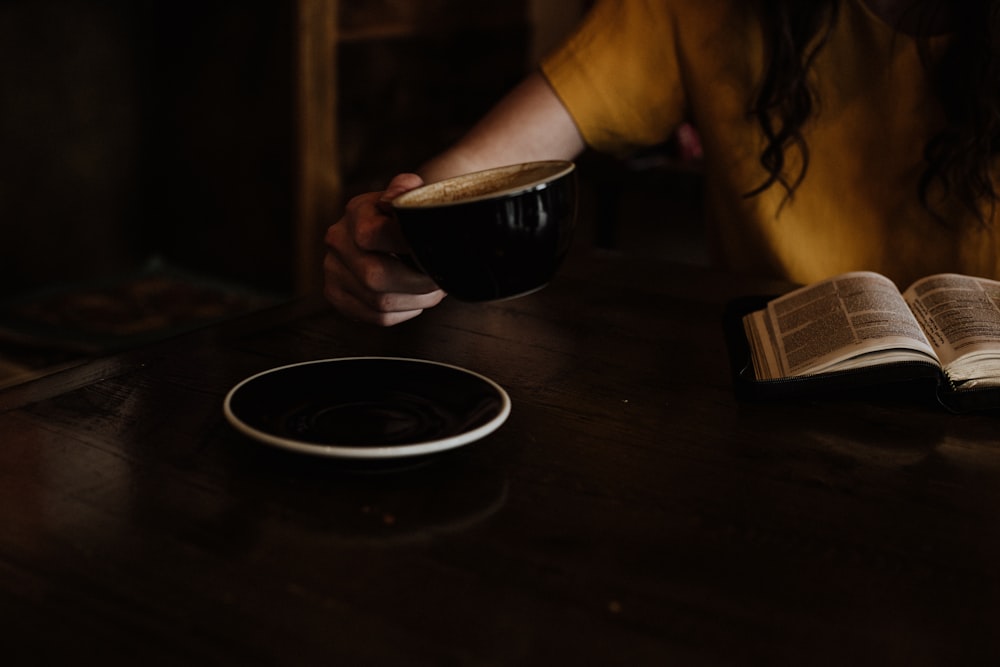 person holding black cup near saucer