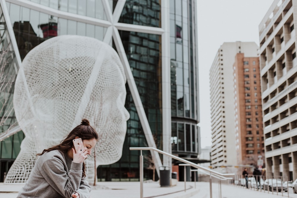 Femme assise sur le sol tenant un smartphone près d’un bâtiment